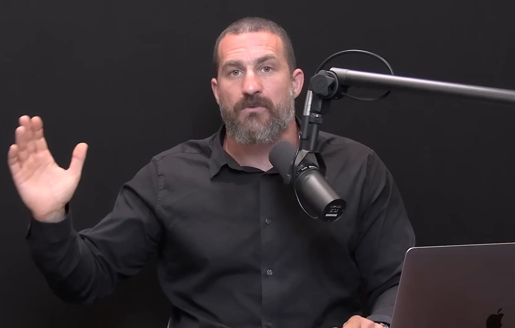 Andrew Huberman explicando en su estudio de grabación, con camisa negra y micrófono