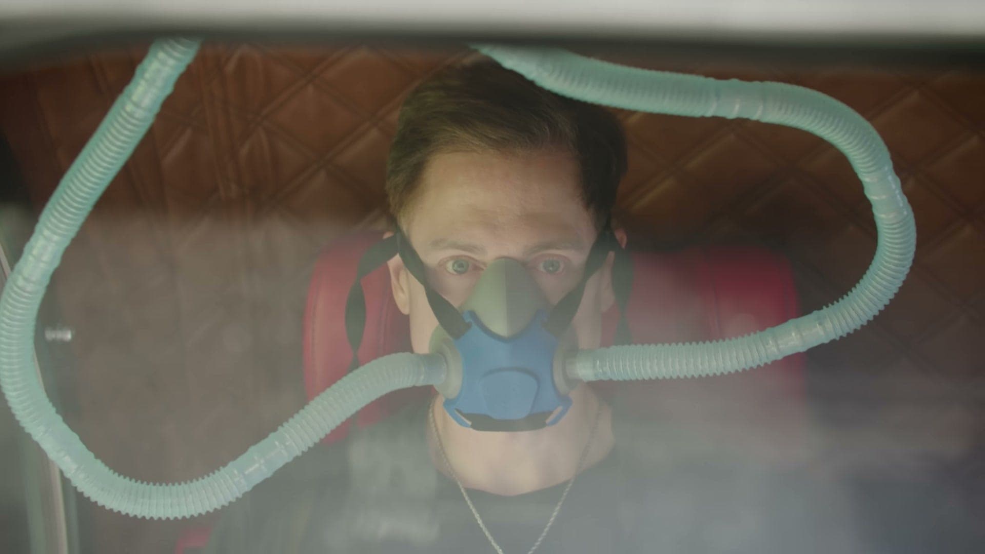 Bryan Johnson con mascarilla de oxígeno, visto a través de la ventana de una cámara hiperbárica